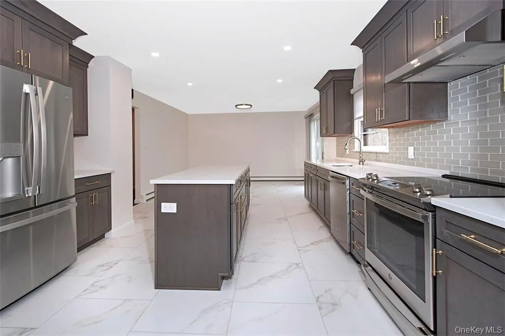 Open kitchen featuring an expansive center island, cabinetry with gold-toned hardware, stainless steel appliances, and a subway tile backsplash Open kitchen featuring an expansive center island, cabinetry with gold-toned hardware, stainless steel appliances, and a subway tile backsplash