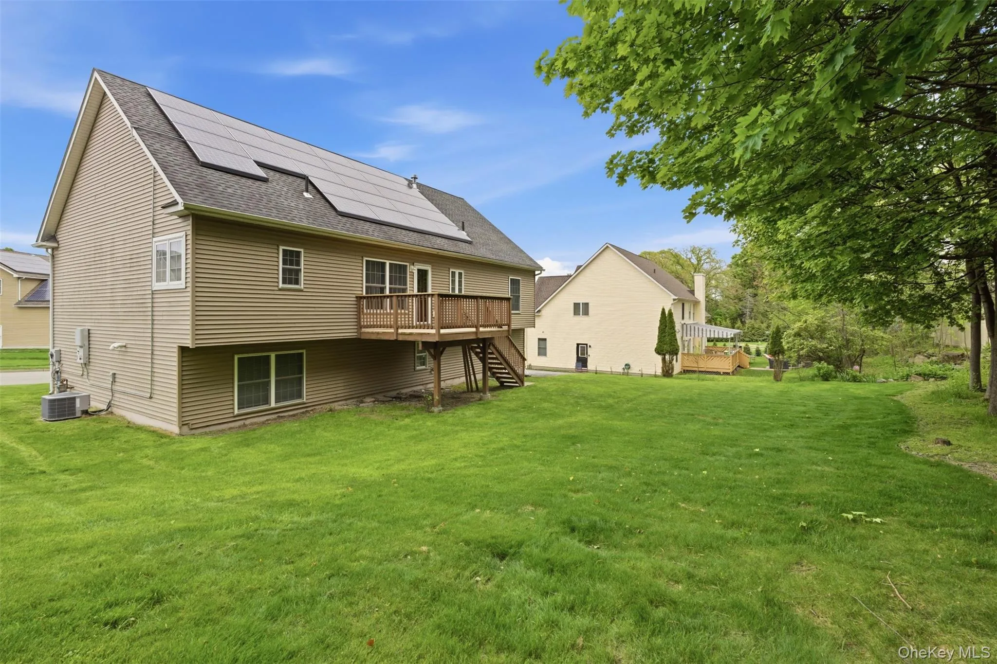 Rear exterior showcasing a spacious green lawn, a wood deck, and solar panels installed on the roof Rear exterior showcasing a spacious green lawn, a wood deck, and solar panels installed on the roof