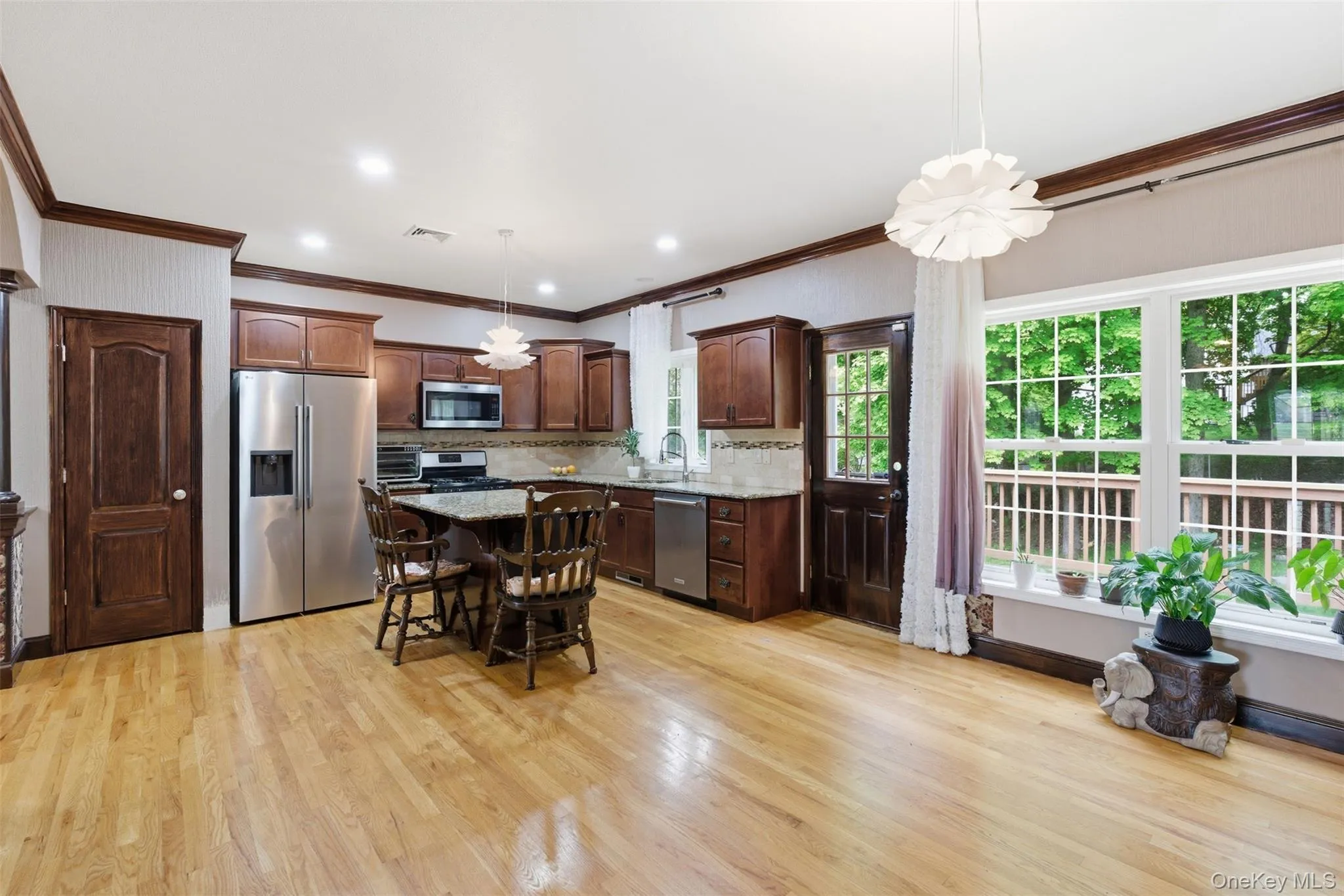 Open-concept kitchen and living area featuring wood-finish flooring, dark wood cabinetry, stainless steel appliances, and a large window with exterior decking Open-concept kitchen and living area featuring wood-finish flooring, dark wood cabinetry, stainless steel appliances, and a large window with exterior decking