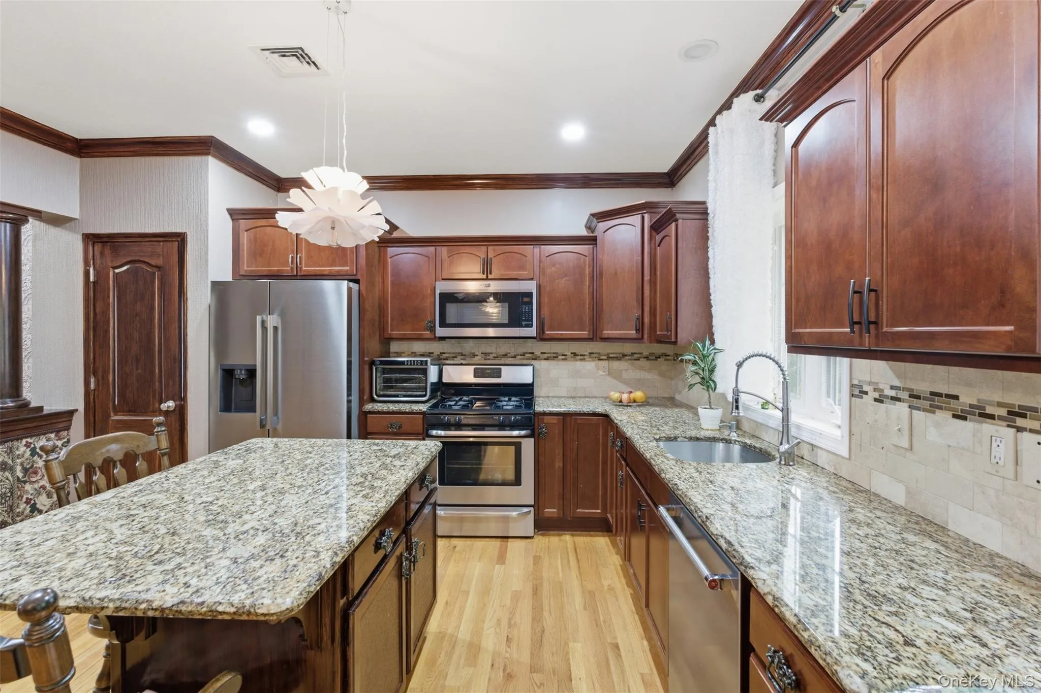 Kitchen featuring wood-finish cabinetry, granite countertops, stainless steel appliances, a center island, and wood-finish flooring Kitchen featuring wood-finish cabinetry, granite countertops, stainless steel appliances, a center island, and wood-finish flooring