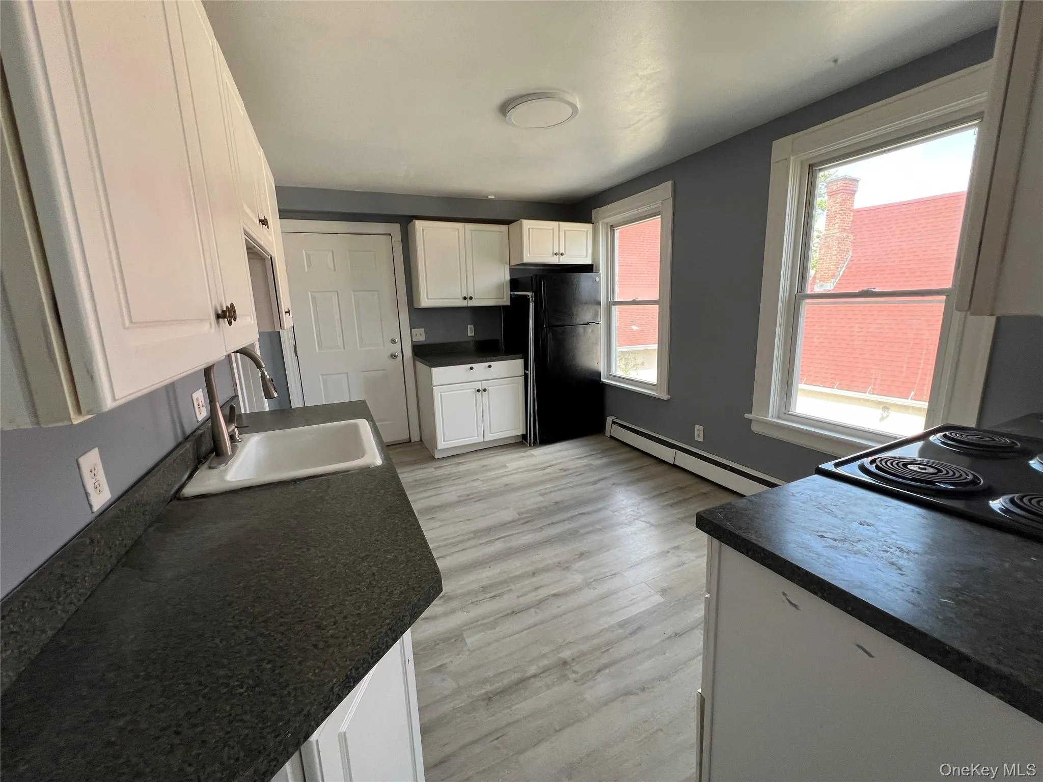 Kitchen featuring white cabinetry, dark countertops, a black refrigerator, and a white sink with a gooseneck faucet Kitchen featuring white cabinetry, dark countertops, a black refrigerator, and a white sink with a gooseneck faucet