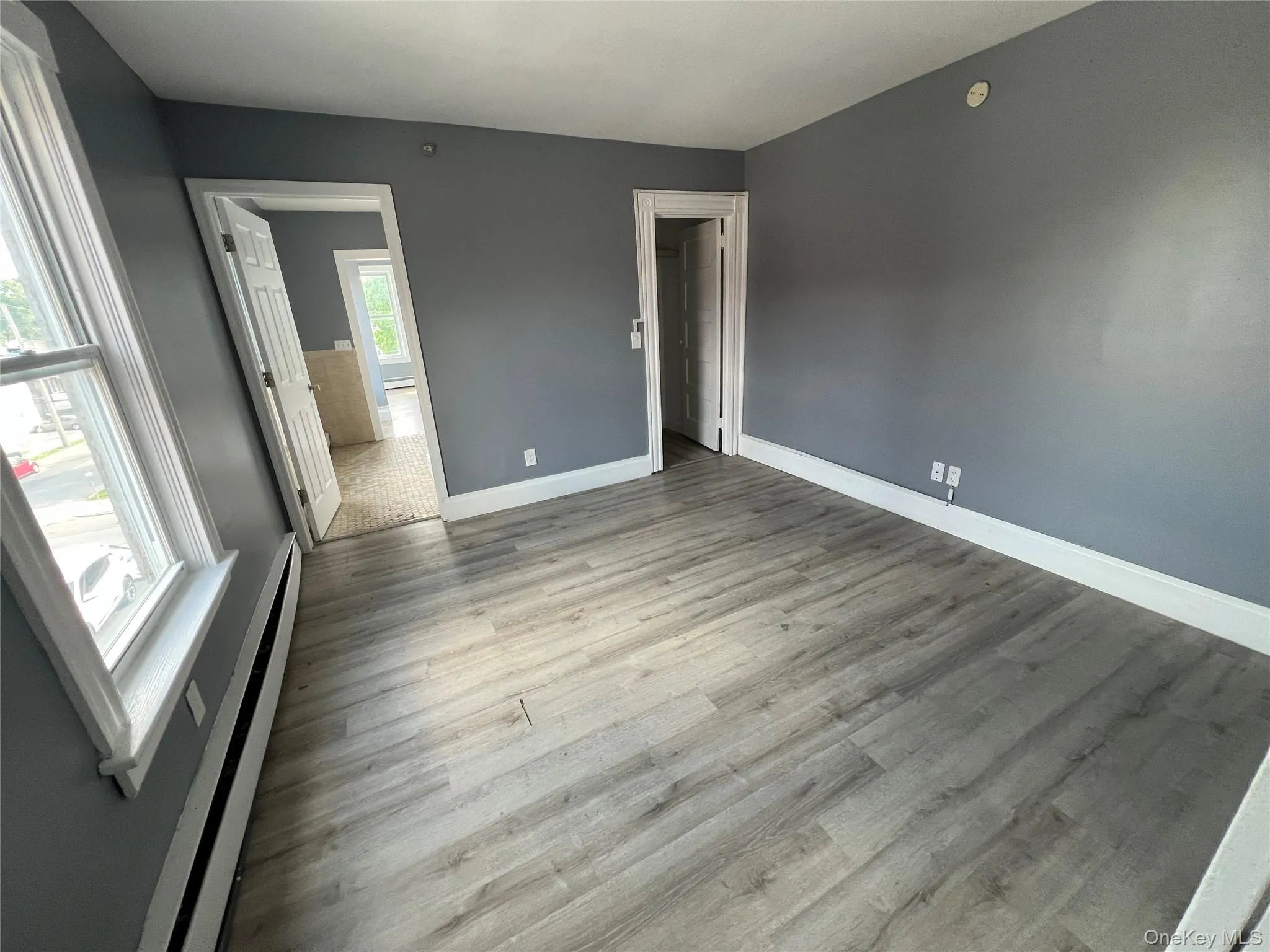 Room featuring light wood-finish flooring, grey painted walls, and white trim Room featuring light wood-finish flooring, grey painted walls, and white trim