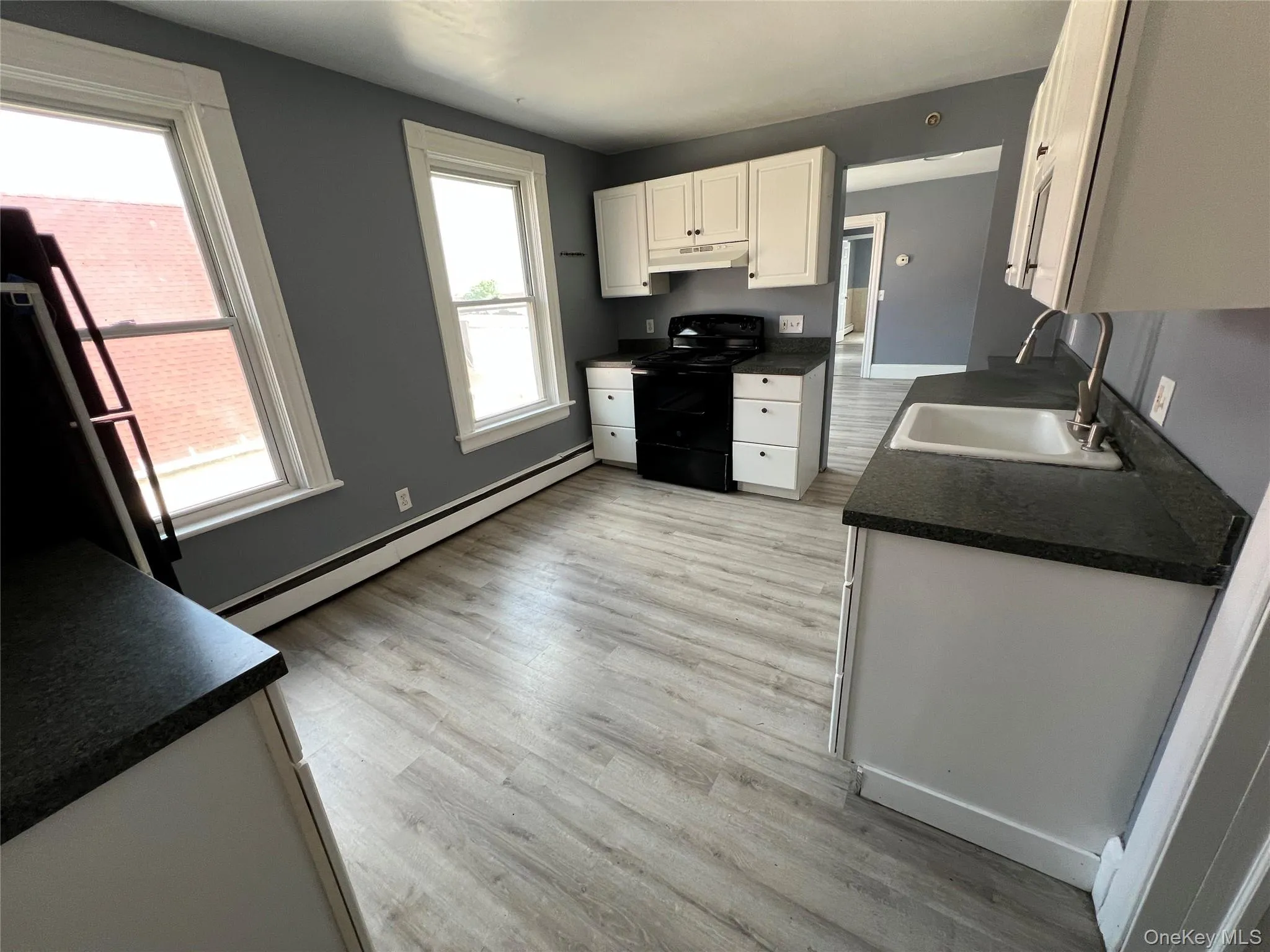Kitchen featuring wood-finish flooring, white cabinetry, dark countertops, and a black range Kitchen featuring wood-finish flooring, white cabinetry, dark countertops, and a black range