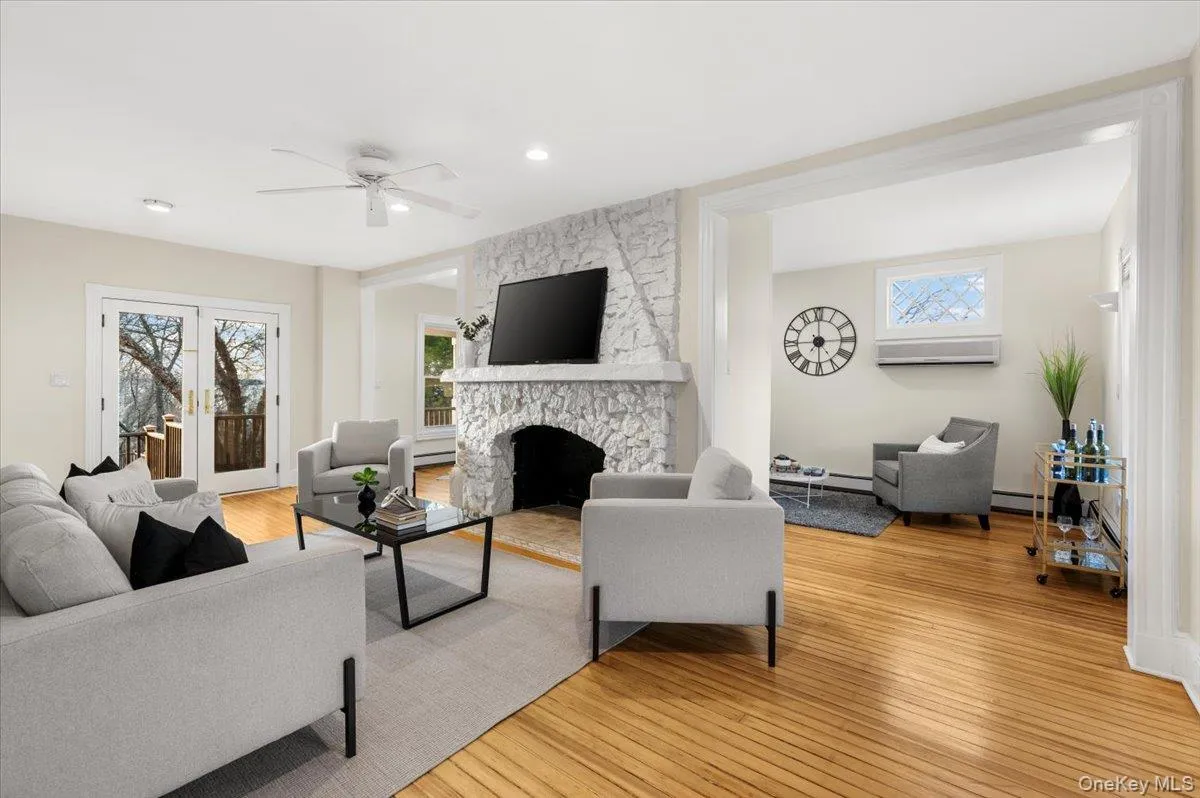 Living room with light wood finished floors, healthy amount of natural light, a stone fireplace, and a ceiling fan Living room with light wood finished floors, healthy amount of natural light, a stone fireplace, and a ceiling fan