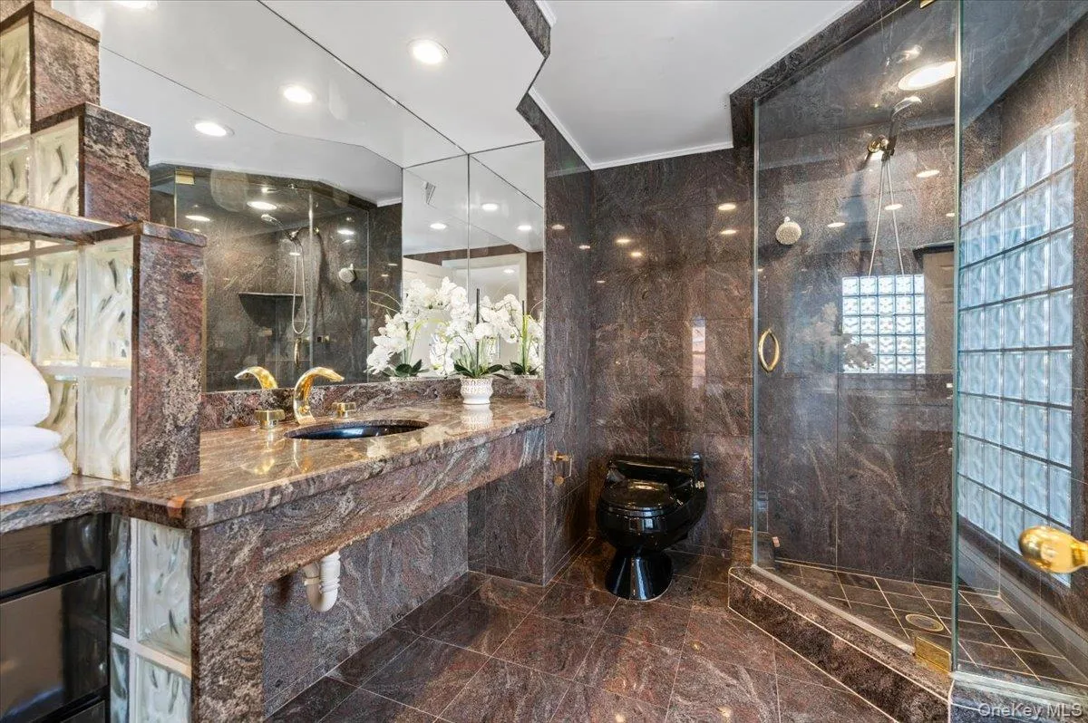 Full bath featuring vanity, tile walls, dark marble finish flooring, ornamental molding, and a marble finish shower Full bath featuring vanity, tile walls, dark marble finish flooring, ornamental molding, and a marble finish shower