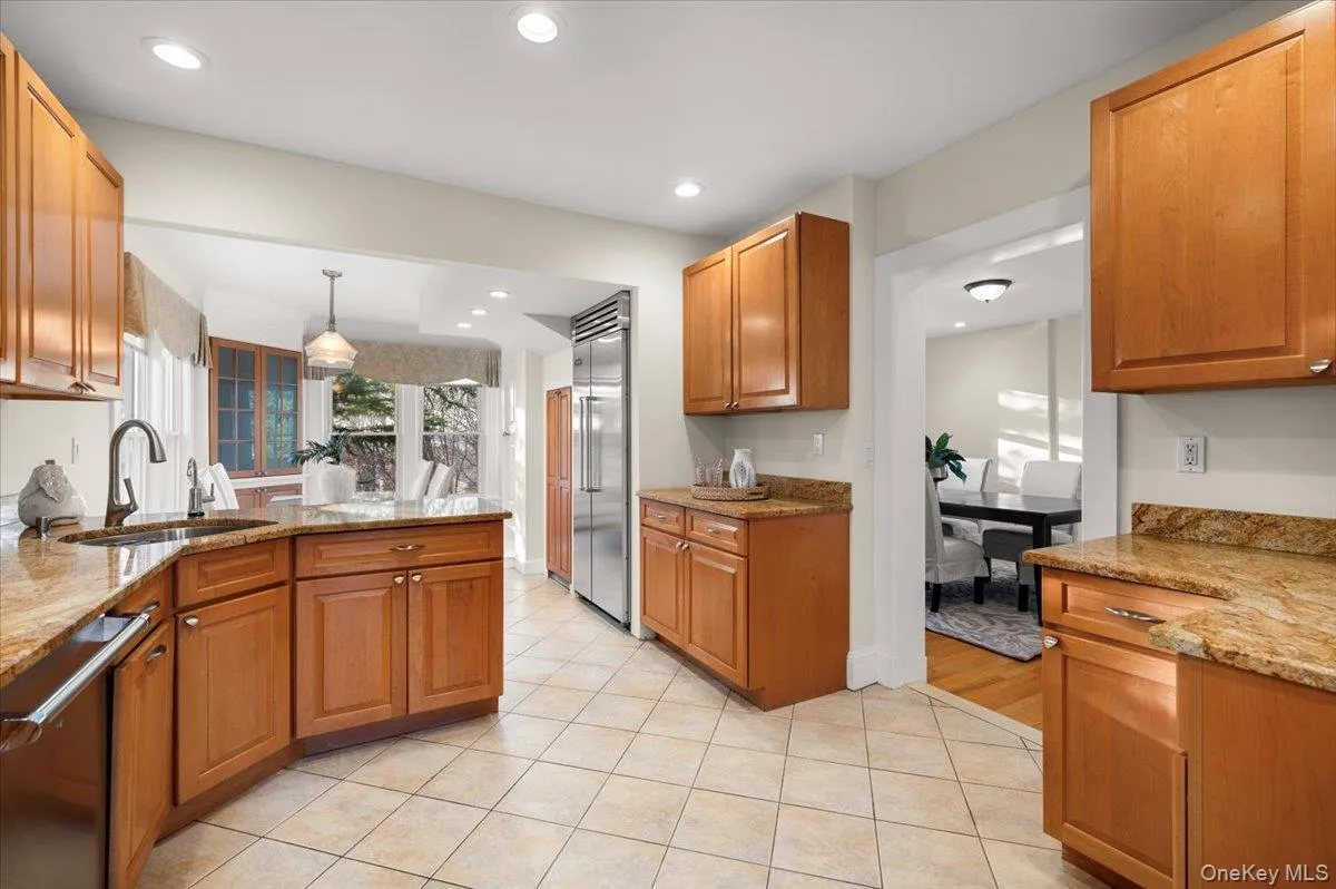 Kitchen with light stone counters, brown cabinets, stainless steel appliances, pendant lighting, and light tile patterned flooring Kitchen with light stone counters, brown cabinets, stainless steel appliances, pendant lighting, and light tile patterned flooring