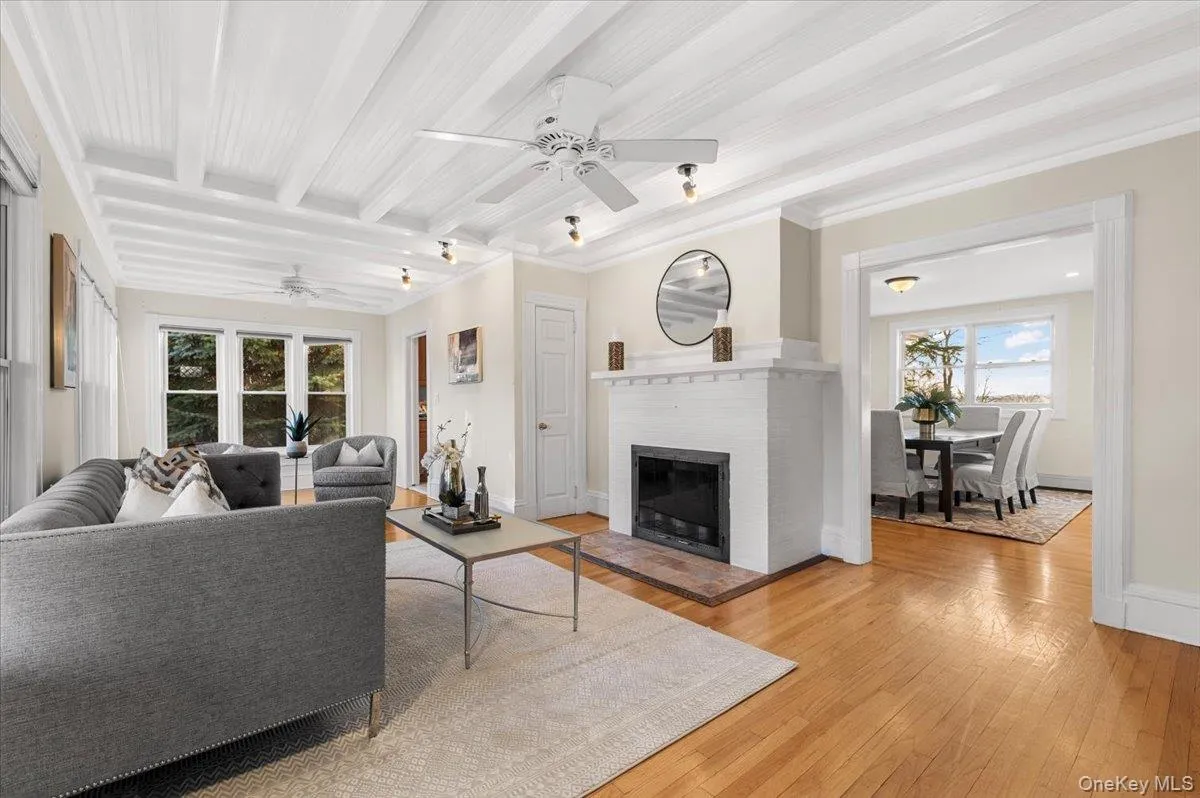 Living area with a fireplace, a ceiling fan, healthy amount of natural light, light wood finished floors, and beam ceiling Living area with a fireplace, a ceiling fan, healthy amount of natural light, light wood finished floors, and beam ceiling