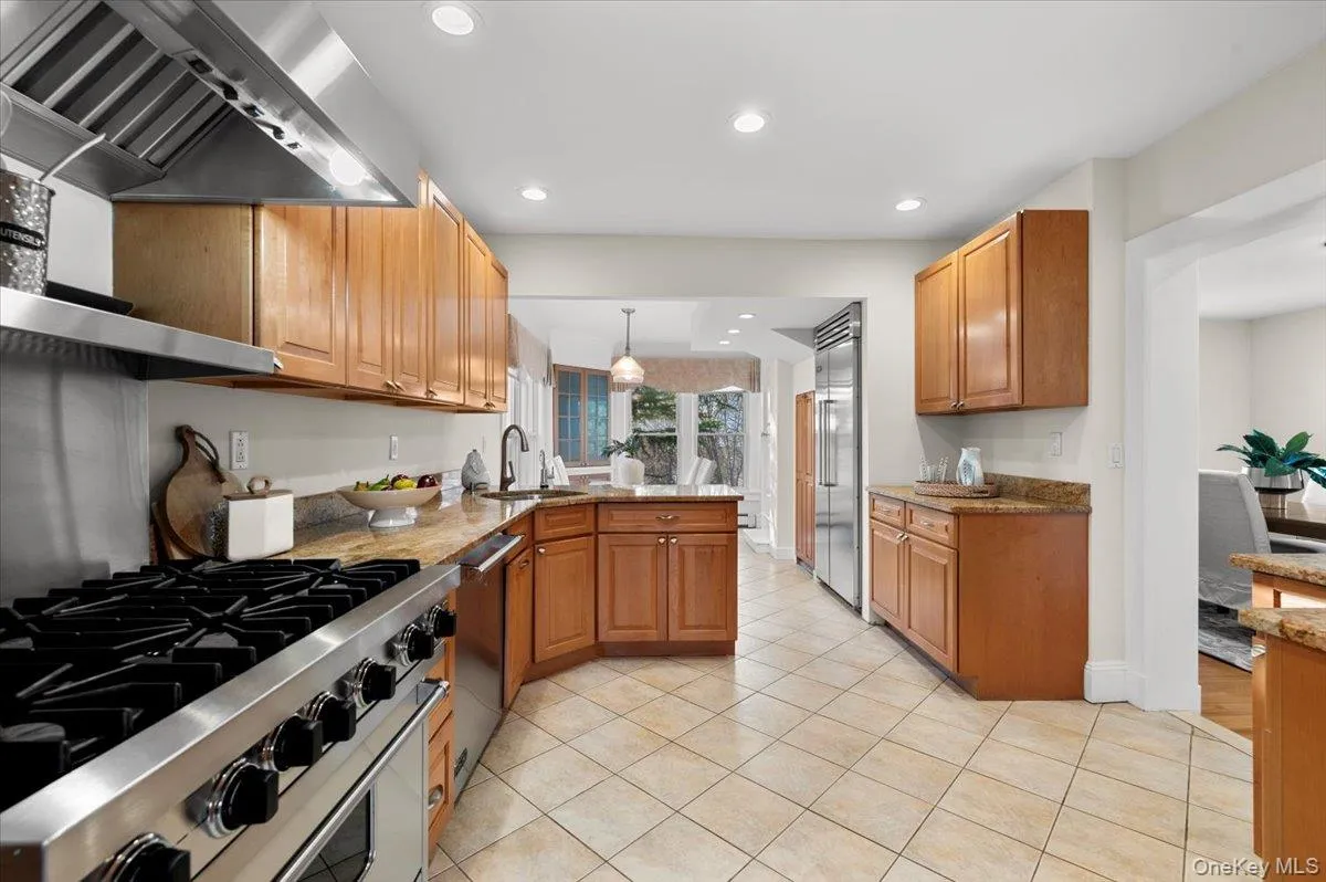 Kitchen with premium appliances, wall chimney exhaust hood, hanging light fixtures, a peninsula, and brown cabinetry Kitchen with premium appliances, wall chimney exhaust hood, hanging light fixtures, a peninsula, and brown cabinetry