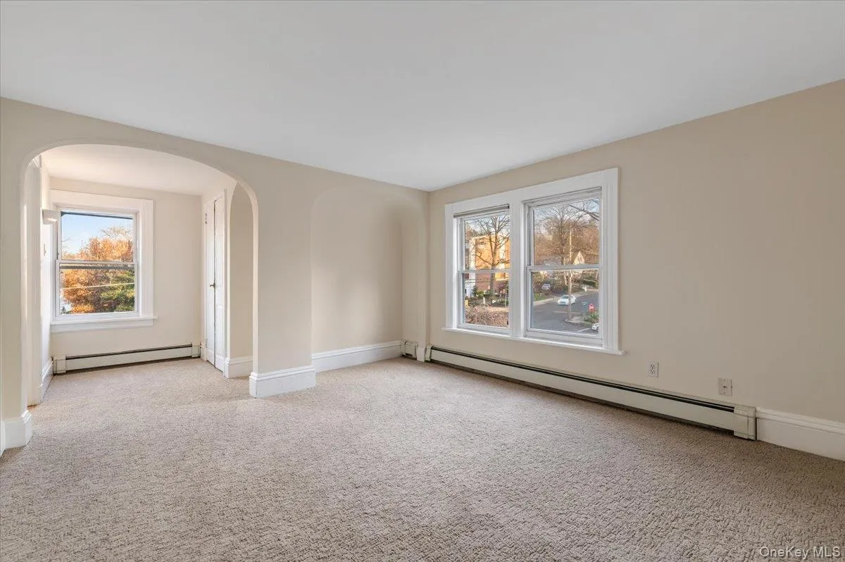 Carpeted spare room with a baseboard radiator, arched walkways, and plenty of natural light Carpeted spare room with a baseboard radiator, arched walkways, and plenty of natural light