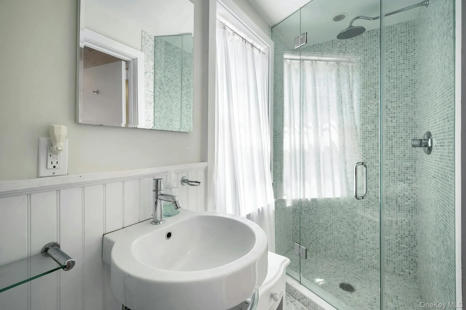 Modern bathroom featuring a glass-enclosed shower with mosaic tile surround, rainfall showerhead, and a pedestal sink with chrome fixtures Modern bathroom featuring a glass-enclosed shower with mosaic tile surround, rainfall showerhead, and a pedestal sink with chrome fixtures