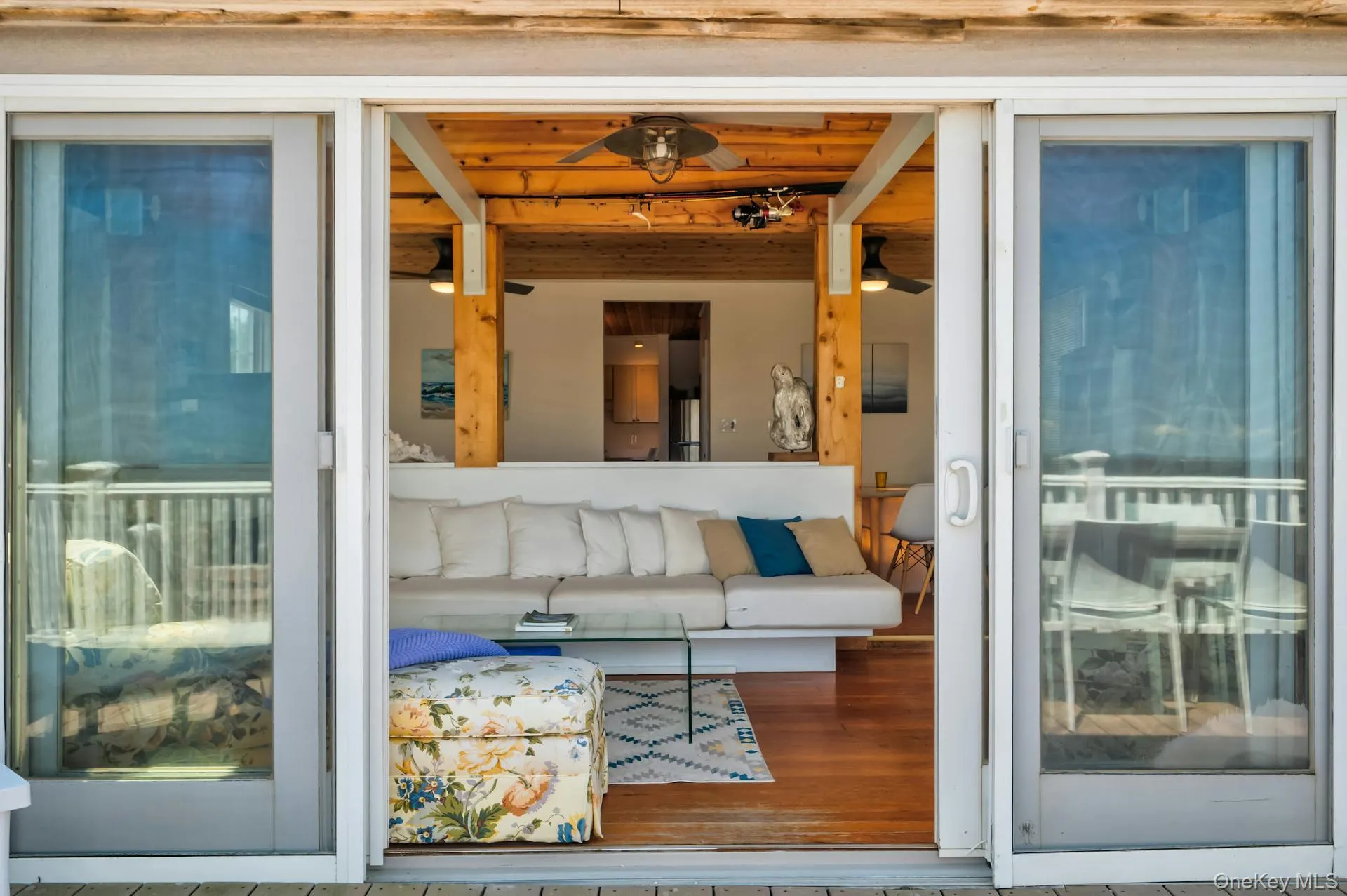 Sliding glass doors opening to an interior space featuring wood-finish flooring, exposed wood ceiling beams, and a white built-in sofa Sliding glass doors opening to an interior space featuring wood-finish flooring, exposed wood ceiling beams, and a white built-in sofa