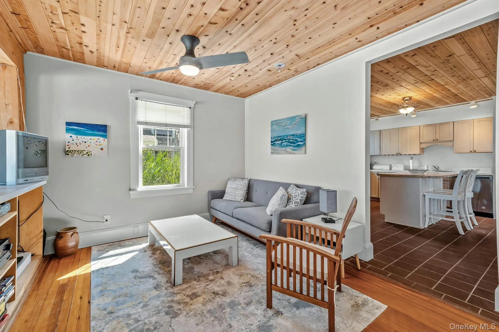Living area featuring a wood-panel ceiling, ceiling fan with integrated lighting, and a window providing natural light Living area featuring a wood-panel ceiling, ceiling fan with integrated lighting, and a window providing natural light