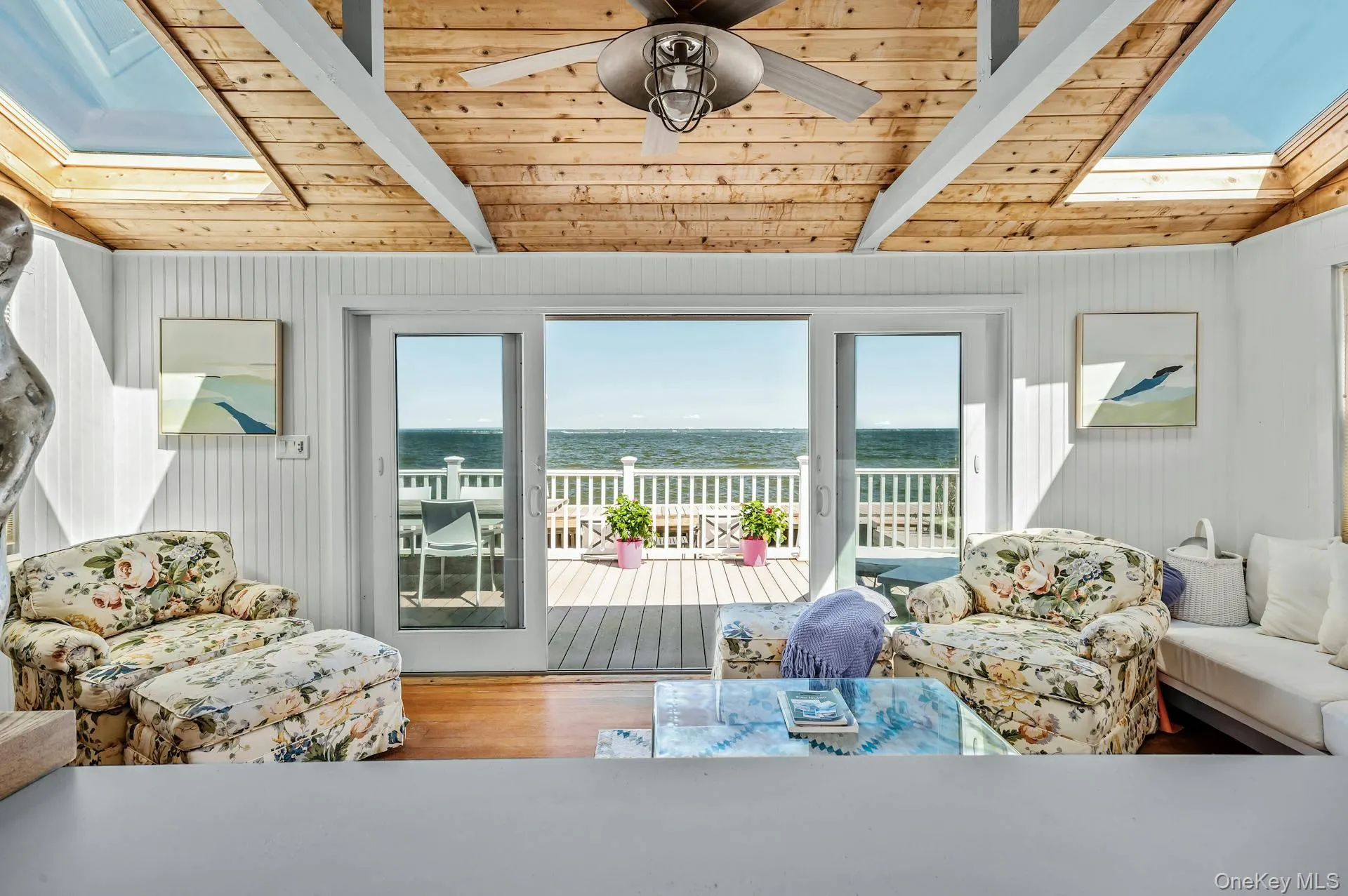 Open-concept room featuring wood-finish flooring, a natural wood paneled ceiling with exposed beams, multiple skylights, and a ceiling fan Open-concept room featuring wood-finish flooring, a natural wood paneled ceiling with exposed beams, multiple skylights, and a ceiling fan