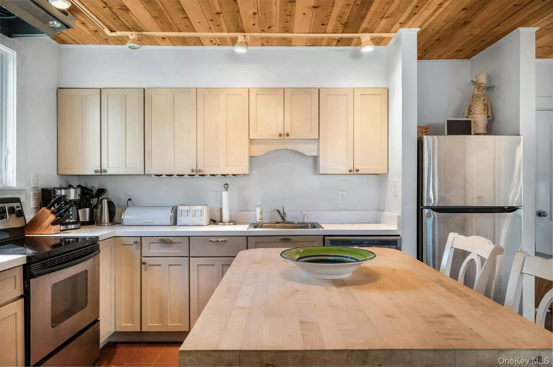 Kitchen featuring a wood-panel ceiling with track lighting, light-toned cabinetry, stainless steel appliances, a built-in dishwasher, and a wood-finish island Kitchen featuring a wood-panel ceiling with track lighting, light-toned cabinetry, stainless steel appliances, a built-in dishwasher, and a wood-finish island