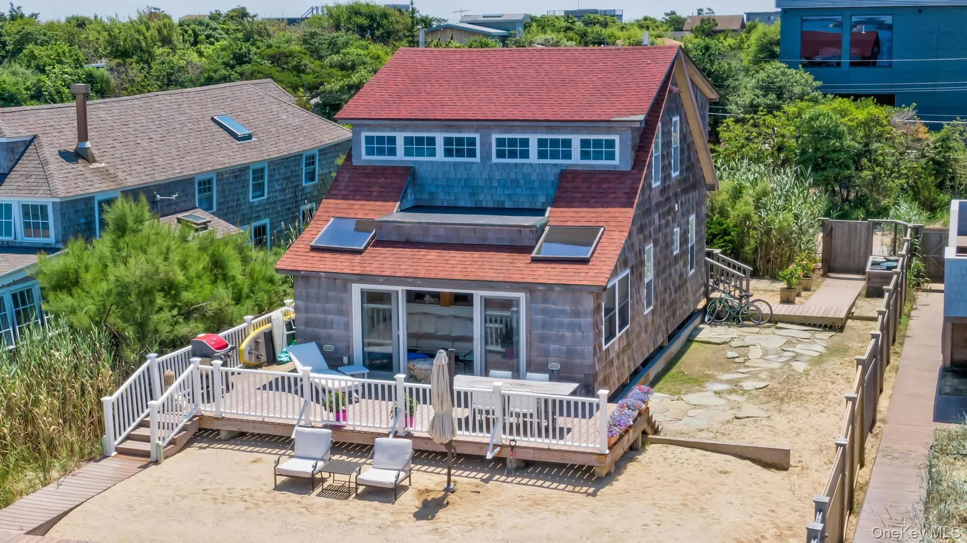 Shingle-sided residence featuring a red gable roof, multiple windows, and a sand-level wood deck Shingle-sided residence featuring a red gable roof, multiple windows, and a sand-level wood deck