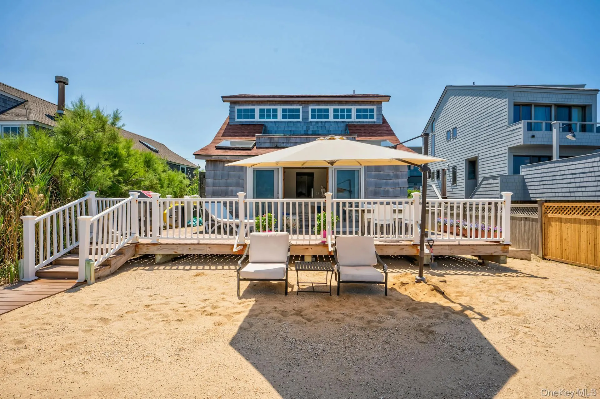 Expansive sandy backyard featuring a wooden deck with white railing, direct access to the interior, and a wooden walkway Expansive sandy backyard featuring a wooden deck with white railing, direct access to the interior, and a wooden walkway