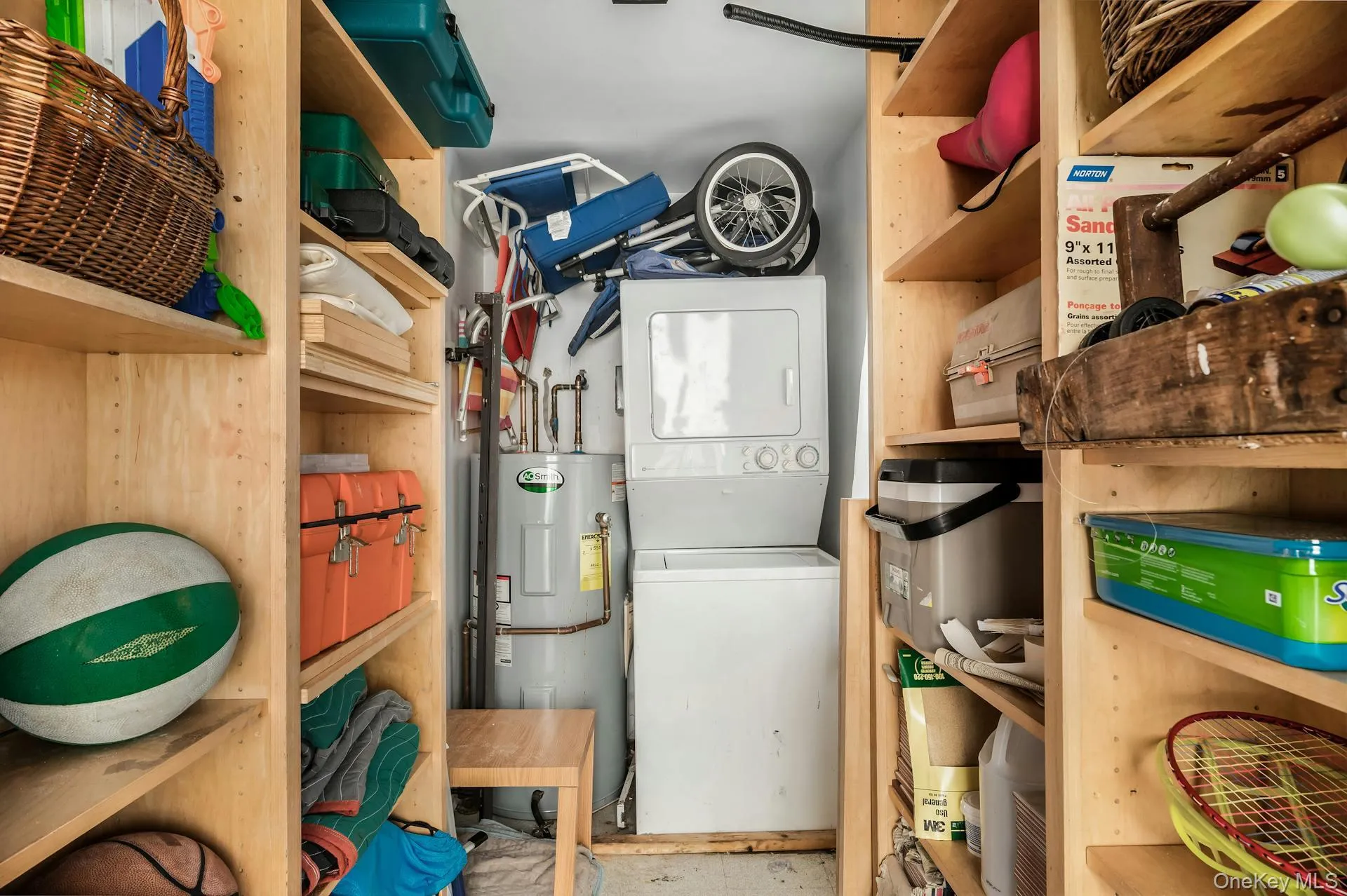 Utility closet featuring a stacked washer and dryer unit, water heater, and built-in shelving Utility closet featuring a stacked washer and dryer unit, water heater, and built-in shelving