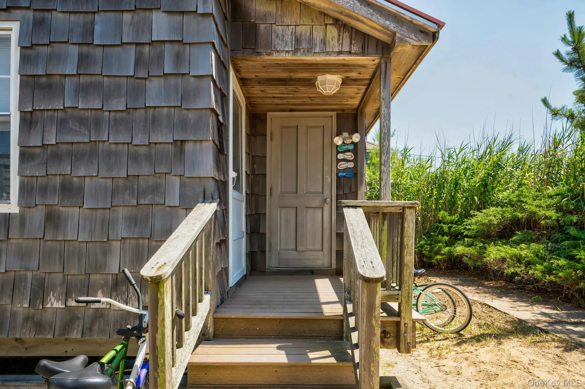 Exterior featuring wood shingle siding, an inviting covered entry porch, a wood-finish door, and natural landscaping with tall grasses Exterior featuring wood shingle siding, an inviting covered entry porch, a wood-finish door, and natural landscaping with tall grasses