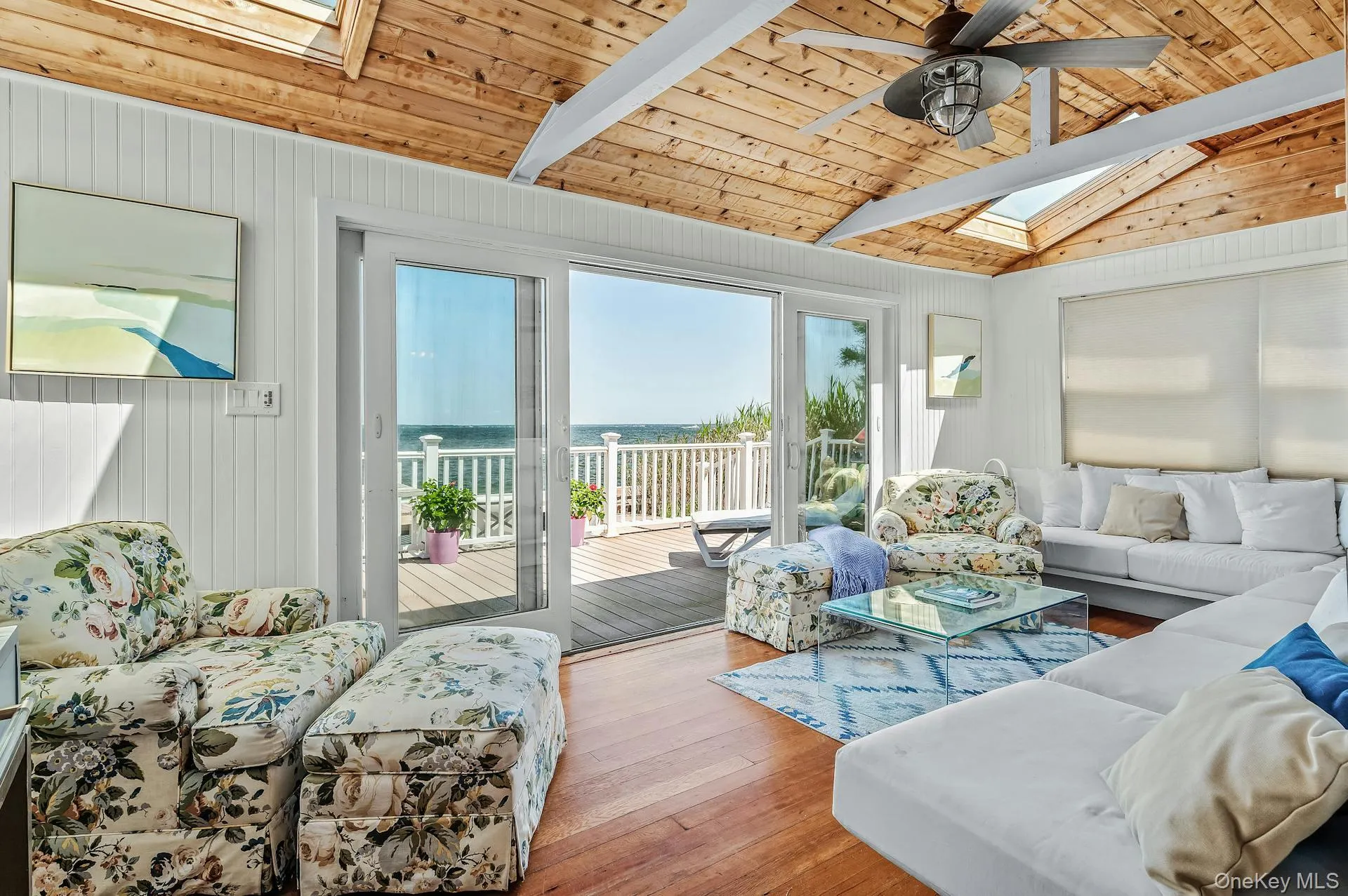 Living area featuring wood-finish flooring, a vaulted wood-paneled ceiling with skylights, and a ceiling fan Living area featuring wood-finish flooring, a vaulted wood-paneled ceiling with skylights, and a ceiling fan