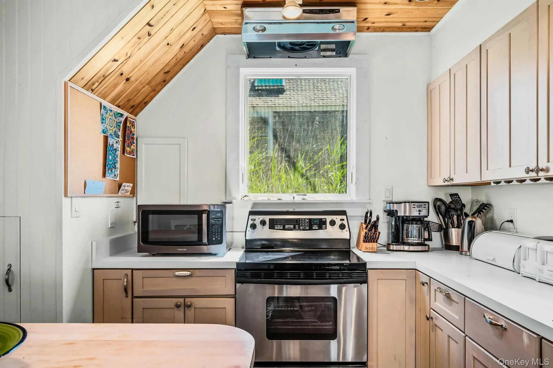 Kitchen featuring wood-paneled sloped ceiling, light-toned cabinetry, light countertops, and a stainless steel electric range Kitchen featuring wood-paneled sloped ceiling, light-toned cabinetry, light countertops, and a stainless steel electric range