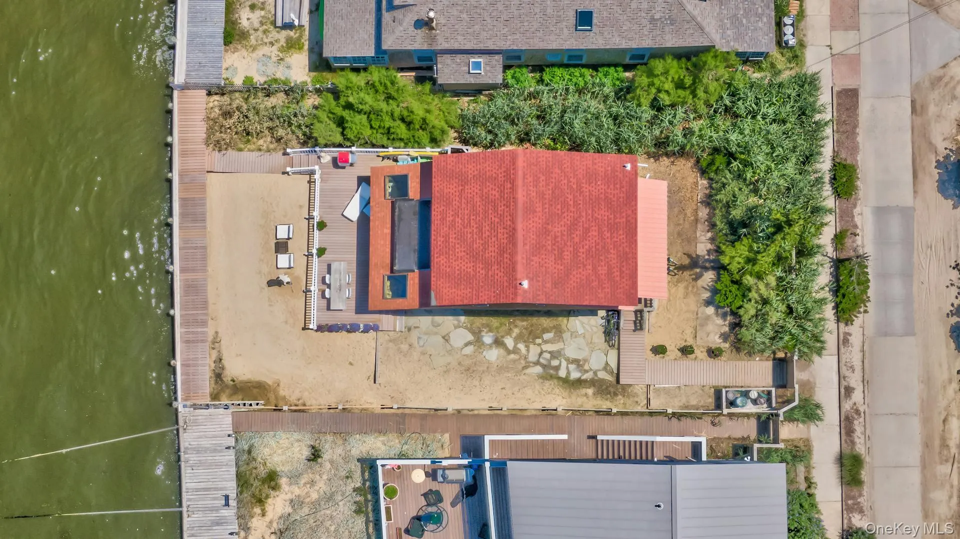 Waterfront property featuring a private dock, expansive deck, sandy beach area, and a red shingle roof Waterfront property featuring a private dock, expansive deck, sandy beach area, and a red shingle roof