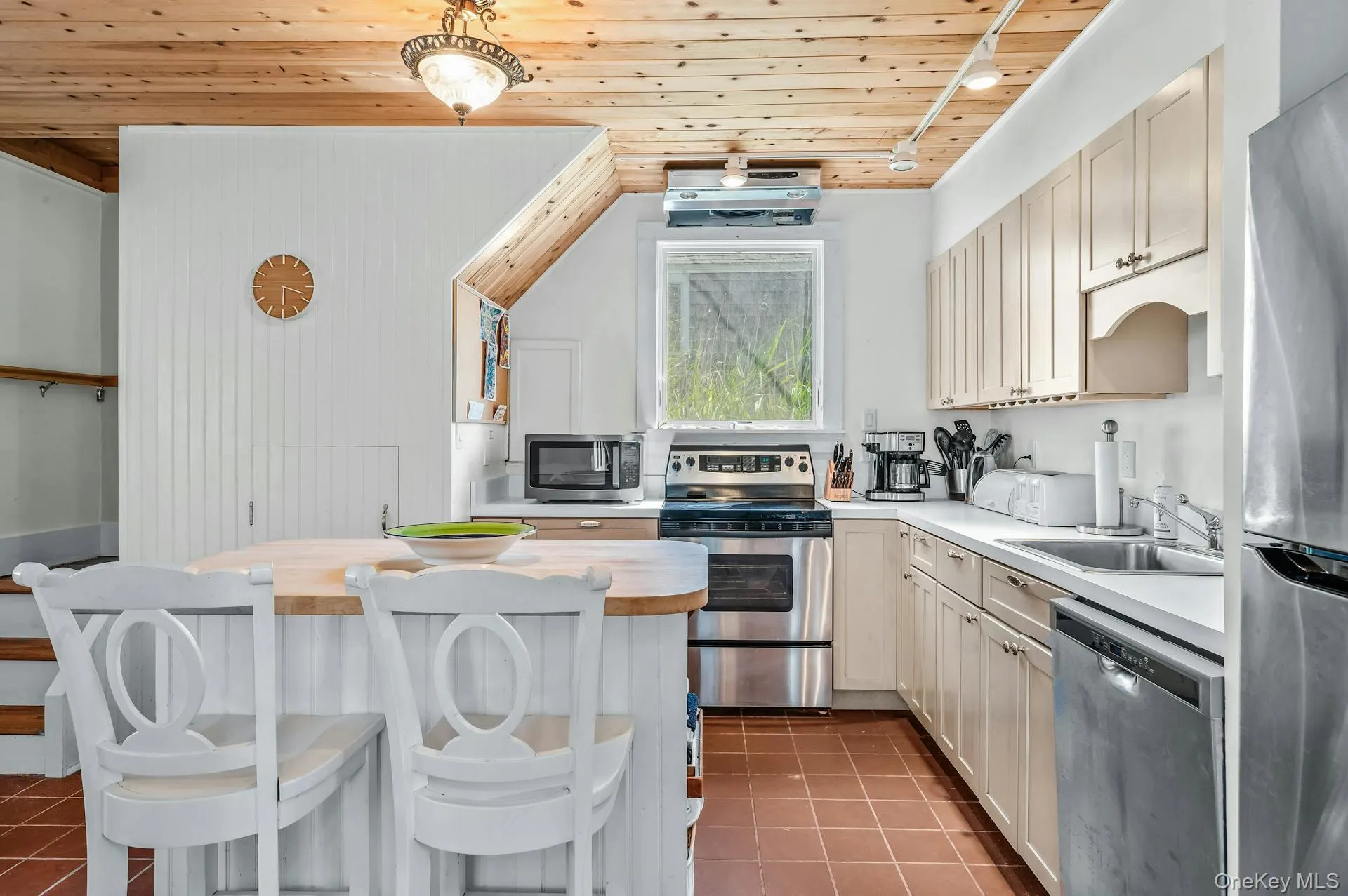 Kitchen featuring wood-paneled ceilings, white cabinetry, stainless steel appliances, and terra cotta floor tiles Kitchen featuring wood-paneled ceilings, white cabinetry, stainless steel appliances, and terra cotta floor tiles