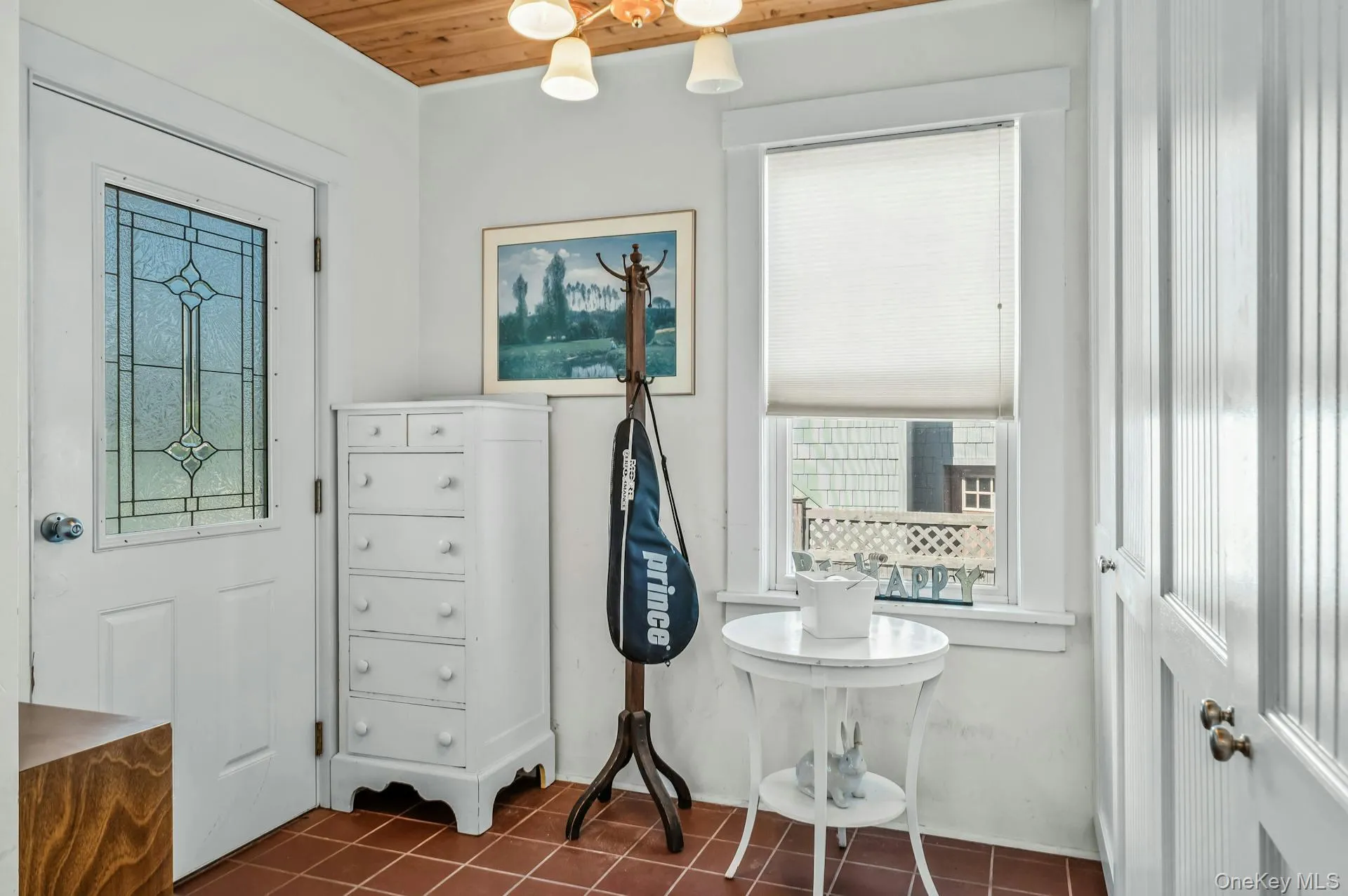 Entry area featuring terracotta-style tile flooring, a wood-paneled ceiling, and a white paneled door with decorative glass Entry area featuring terracotta-style tile flooring, a wood-paneled ceiling, and a white paneled door with decorative glass