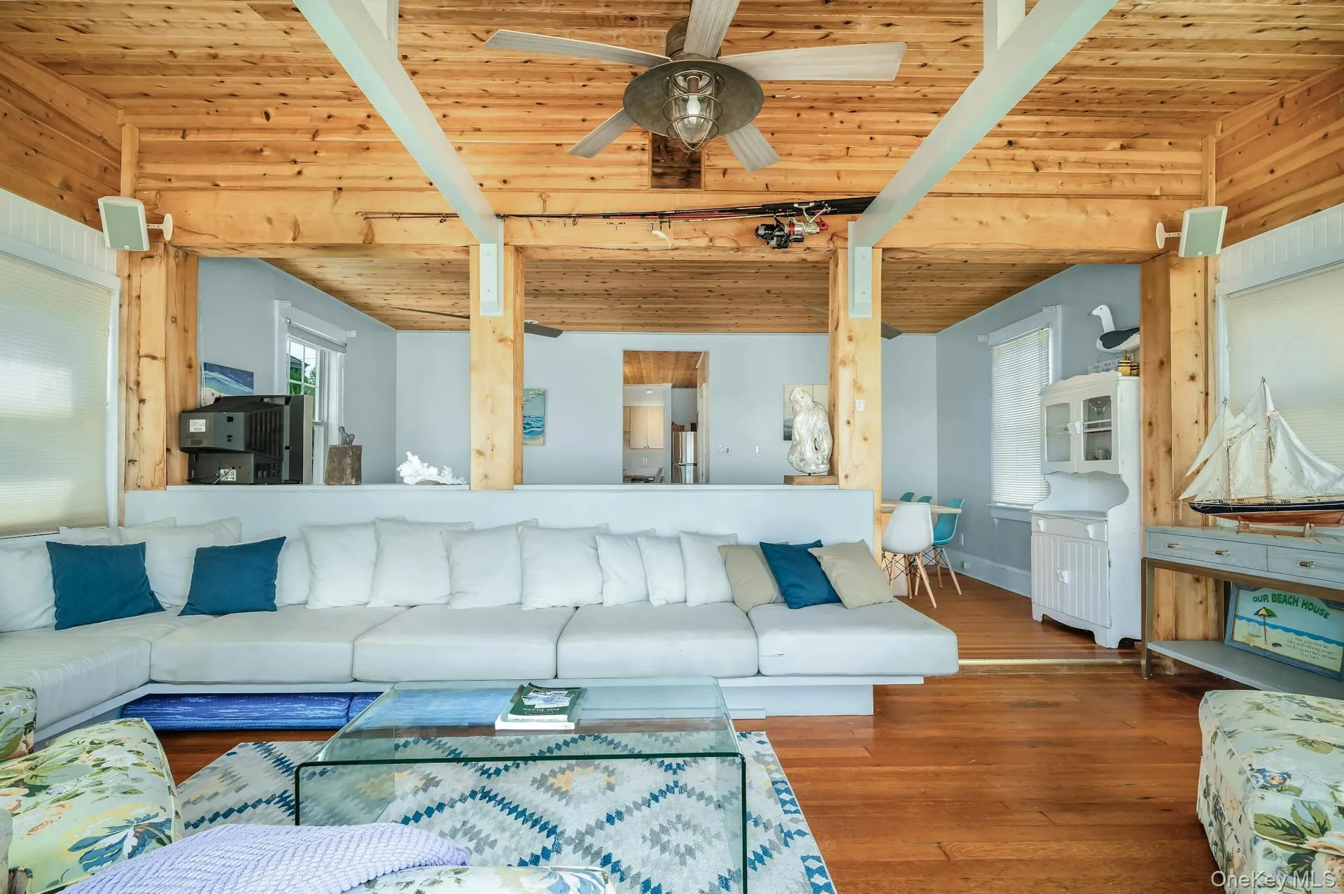 Open-concept living area featuring wood-finish flooring, exposed wooden beams, and a wood-slat ceiling with a ceiling fan Open-concept living area featuring wood-finish flooring, exposed wooden beams, and a wood-slat ceiling with a ceiling fan