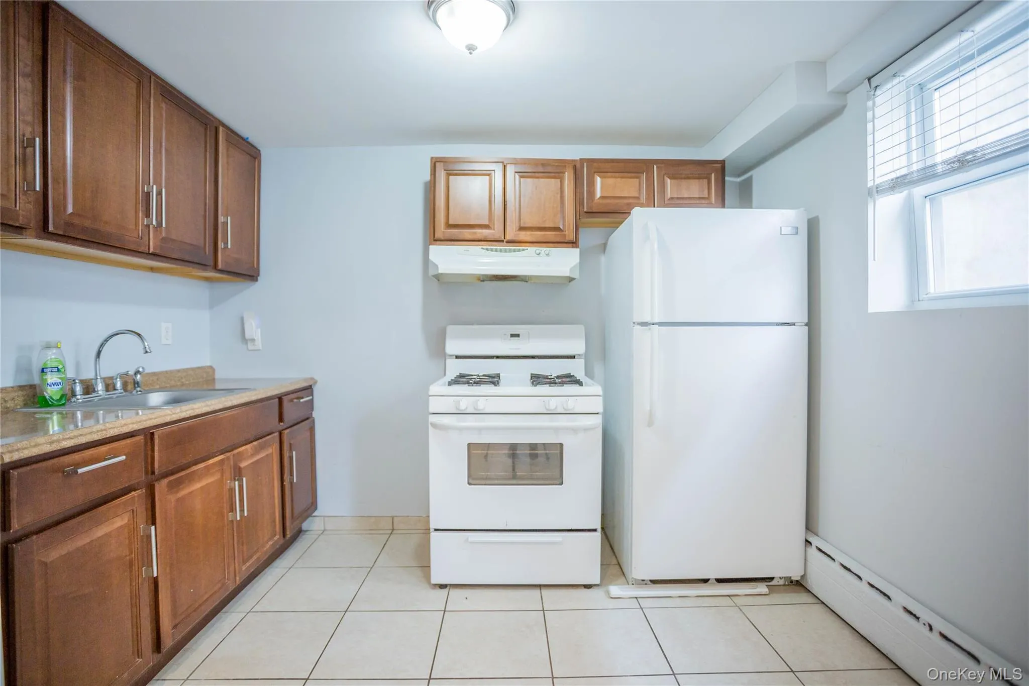 Kitchen featuring a baseboard heating unit, white appliances, light tile patterned floors, under cabinet range hood, and a sink Kitchen featuring a baseboard heating unit, white appliances, light tile patterned floors, under cabinet range hood, and a sink