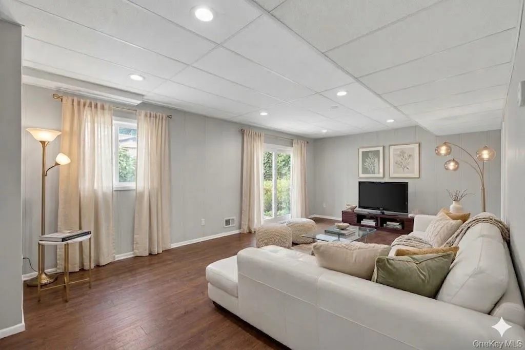 Spacious living area featuring wood-finish flooring, recessed lighting, and light gray wall paneling Spacious living area featuring wood-finish flooring, recessed lighting, and light gray wall paneling