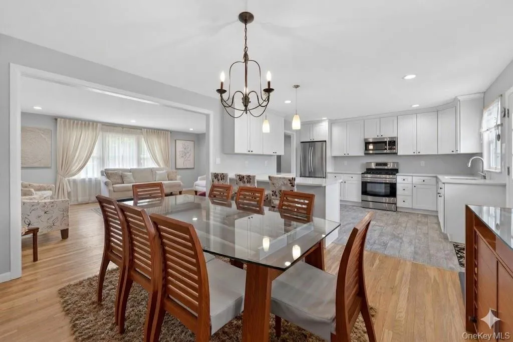 Open-concept dining area featuring a chandelier, wood-finish flooring, and a broad pass-through to a living area Open-concept dining area featuring a chandelier, wood-finish flooring, and a broad pass-through to a living area