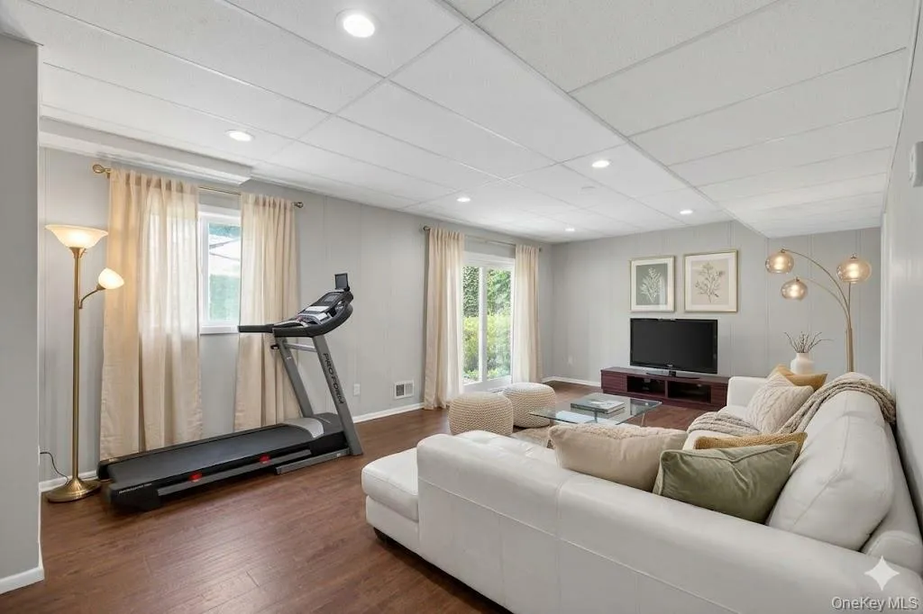Spacious lower-level living area featuring wood-finish flooring, recessed lighting, and light gray paneled walls Spacious lower-level living area featuring wood-finish flooring, recessed lighting, and light gray paneled walls
