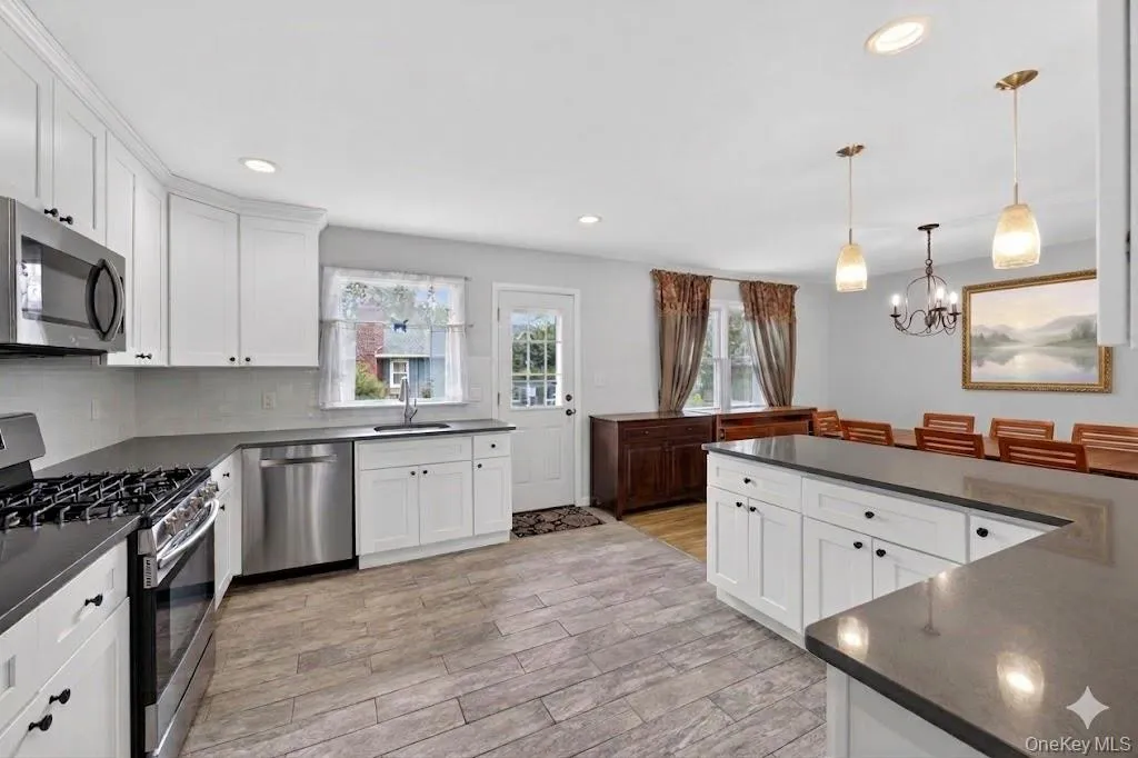 Kitchen featuring white cabinetry, dark countertops, stainless steel appliances, and wood-finish flooring Kitchen featuring white cabinetry, dark countertops, stainless steel appliances, and wood-finish flooring