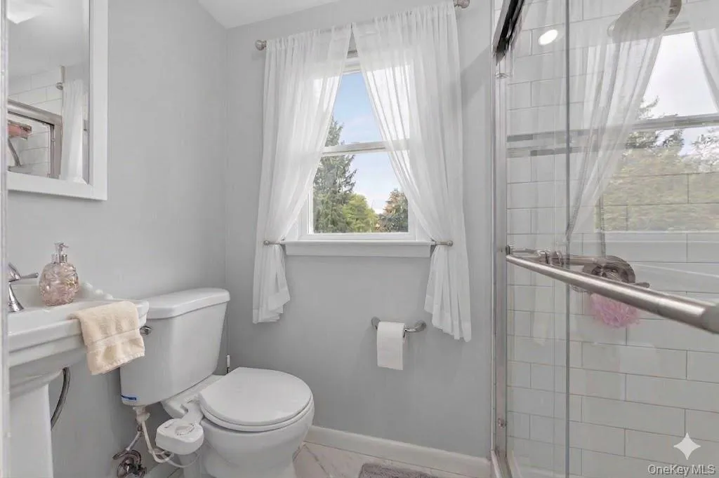 Bathroom featuring a glass-enclosed shower with white subway tile, a white pedestal sink, and a white toilet Bathroom featuring a glass-enclosed shower with white subway tile, a white pedestal sink, and a white toilet