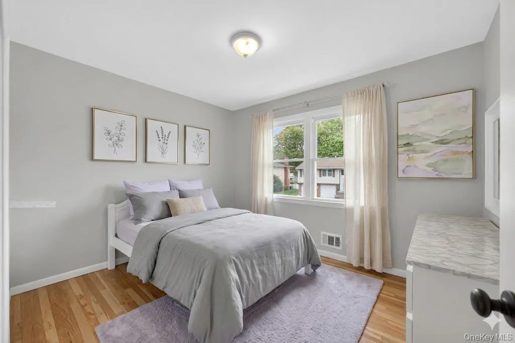 Spacious room featuring wood-finish flooring, light grey wall paint, and a multi-pane window with white trim Spacious room featuring wood-finish flooring, light grey wall paint, and a multi-pane window with white trim