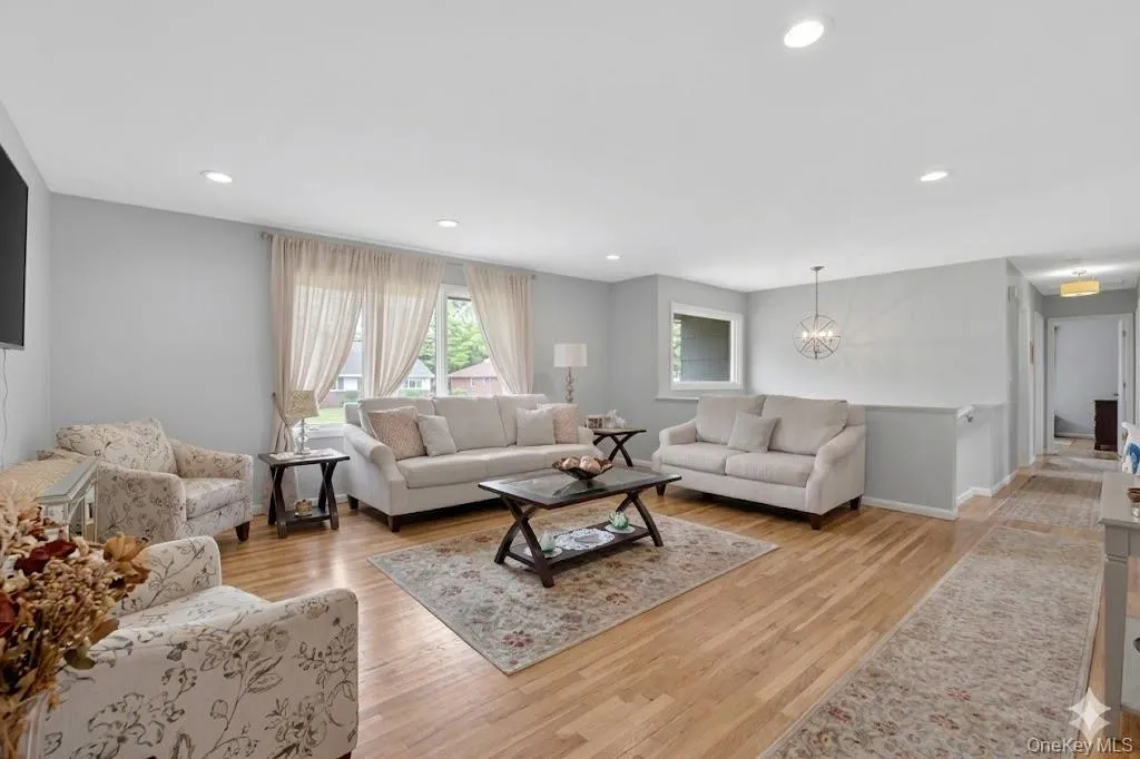 Open concept living area featuring wood-finish flooring, recessed lighting, and a modern chandelier Open concept living area featuring wood-finish flooring, recessed lighting, and a modern chandelier