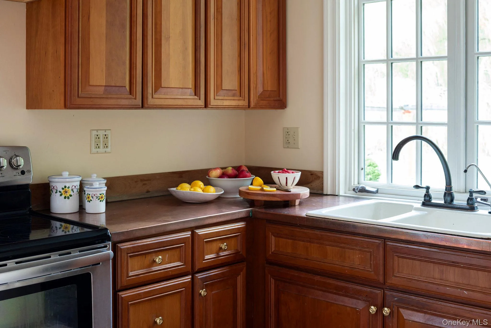 Kitchen with stainless steel range with electric cooktop, dark countertops, and brown cabinetry Kitchen with stainless steel range with electric cooktop, dark countertops, and brown cabinetry