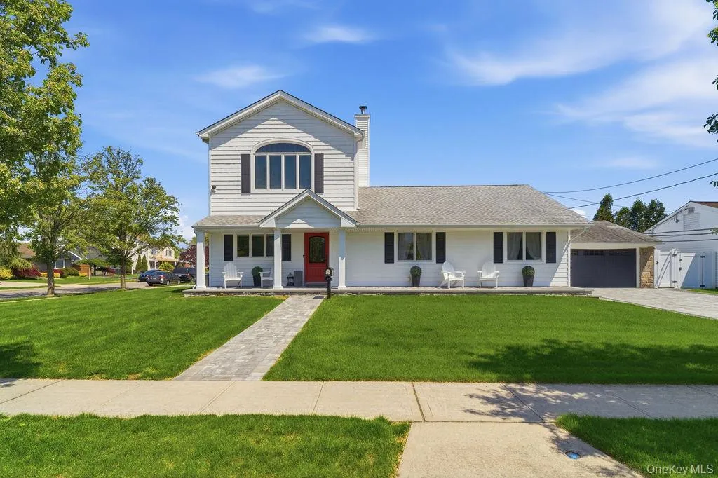 White siding exterior with a red entry door, a covered porch with white columns, and a paved walkway White siding exterior with a red entry door, a covered porch with white columns, and a paved walkway