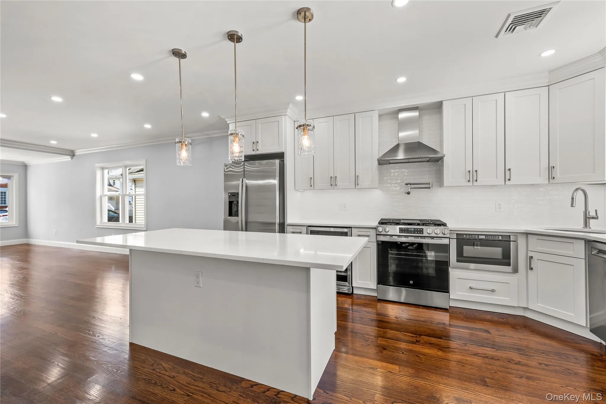 Modern kitchen featuring a large central island with a quartz countertop, stainless steel appliances, white timeless cabinetry, and premium oak flooring with modern stain Modern kitchen featuring a large central island with a quartz countertop, stainless steel appliances, white timeless cabinetry, and premium oak flooring with modern stain