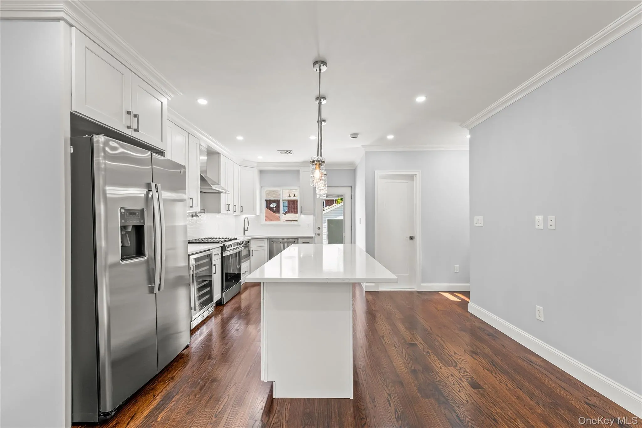 Spacious kitchen featuring white cabinetry, stainless steel appliances, a center island with a light-toned countertop, recessed lighting, and wood-finish flooring Spacious kitchen featuring white cabinetry, stainless steel appliances, a center island with a light-toned countertop, recessed lighting, and wood-finish flooring