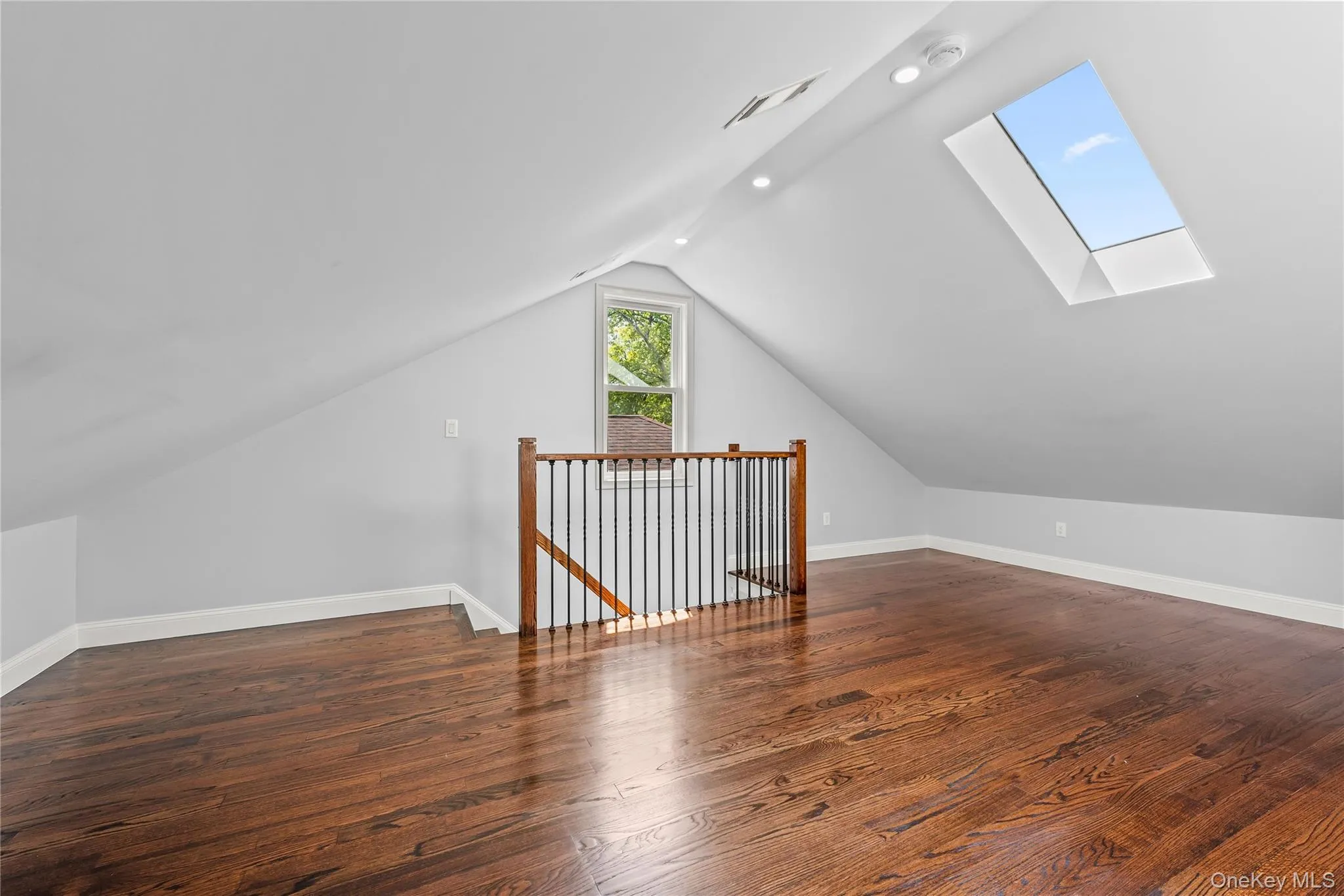 Open concept loft featuring rich wood-finish flooring, a skylight, recessed lighting, and a window with natural light Open concept loft featuring rich wood-finish flooring, a skylight, recessed lighting, and a window with natural light