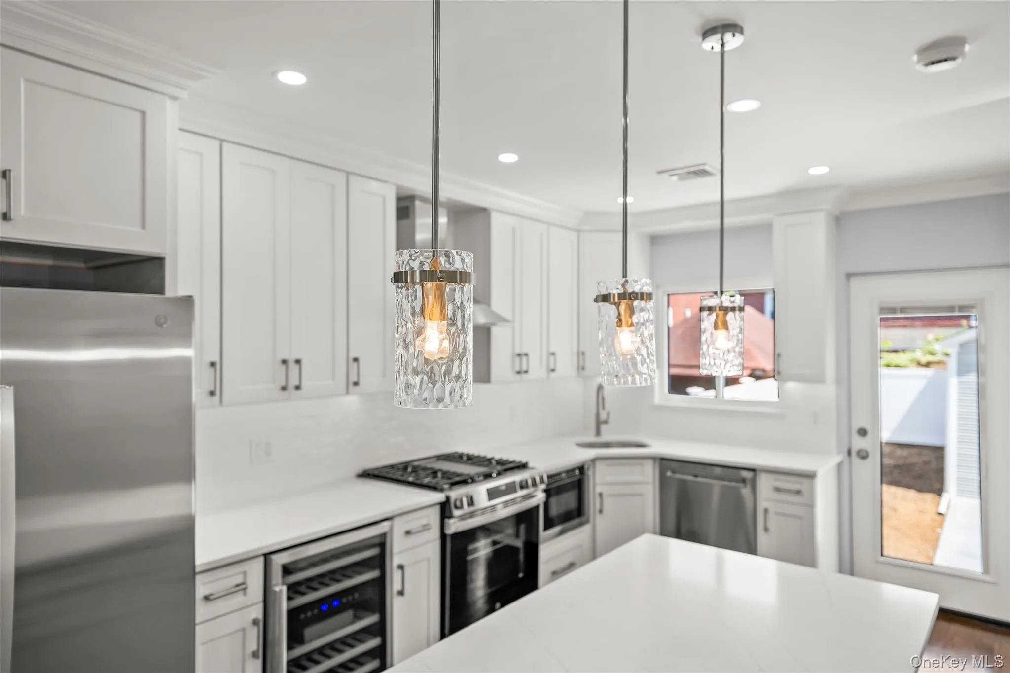 Modern kitchen featuring white shaker cabinetry, stainless steel appliances, white countertops, and three decorative pendant lights Modern kitchen featuring white shaker cabinetry, stainless steel appliances, white countertops, and three decorative pendant lights