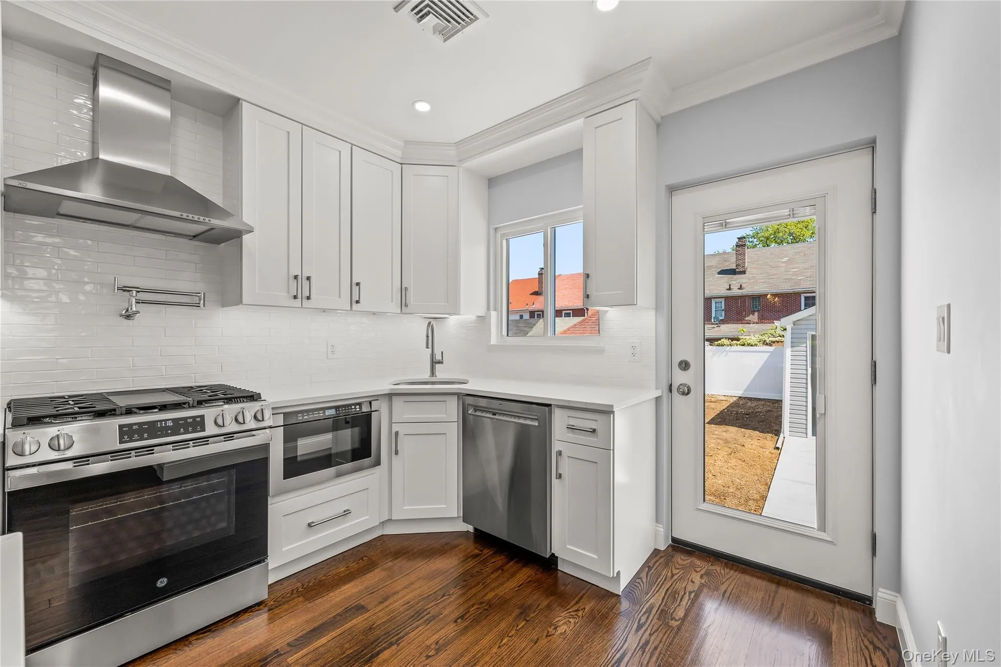 Contemporary kitchen featuring white cabinetry, stainless steel appliances, white subway tile backsplash, and dark wood-finish flooring Contemporary kitchen featuring white cabinetry, stainless steel appliances, white subway tile backsplash, and dark wood-finish flooring