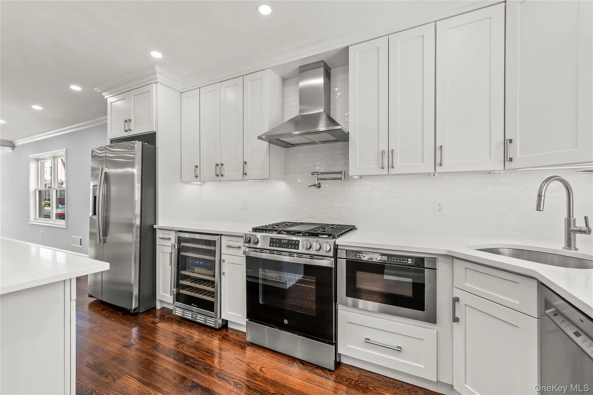 Kitchen featuring white cabinetry, stainless steel appliances, white subway tile backsplash, and wood-finish flooring Kitchen featuring white cabinetry, stainless steel appliances, white subway tile backsplash, and wood-finish flooring