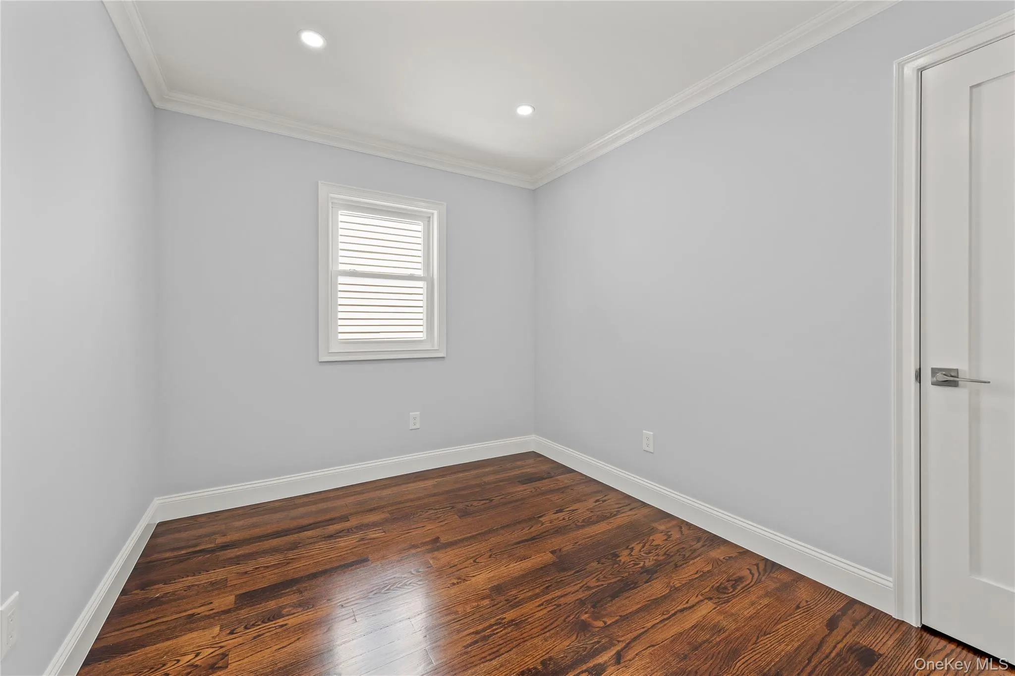 Room featuring wood-finish flooring, white baseboards, crown molding, and recessed lighting Room featuring wood-finish flooring, white baseboards, crown molding, and recessed lighting