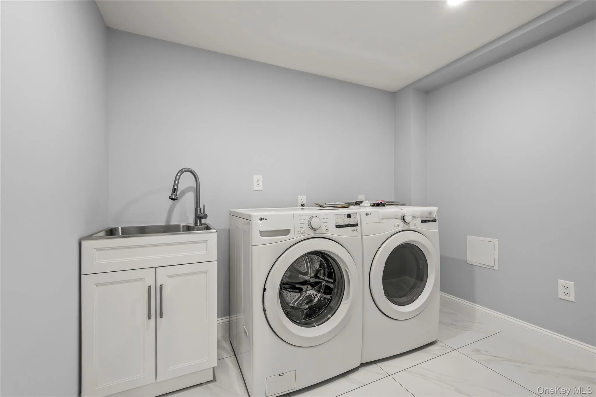 Dedicated laundry area featuring a utility sink with a chrome faucet, white cabinetry, and front-loading appliances Dedicated laundry area featuring a utility sink with a chrome faucet, white cabinetry, and front-loading appliances