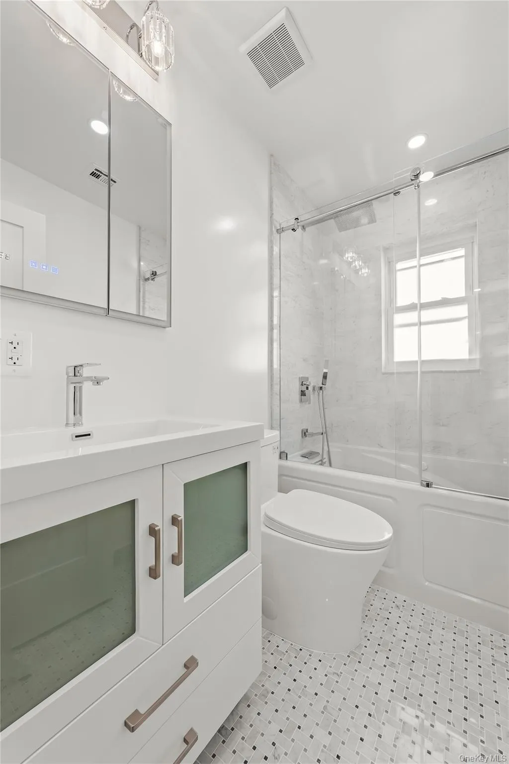 Bathroom featuring a white vanity with frosted glass cabinet doors, a full-size jacuzzi bathtub with sliding glass enclosure, white marble tile surround, and a window Bathroom featuring a white vanity with frosted glass cabinet doors, a full-size jacuzzi bathtub with sliding glass enclosure, white marble tile surround, and a window