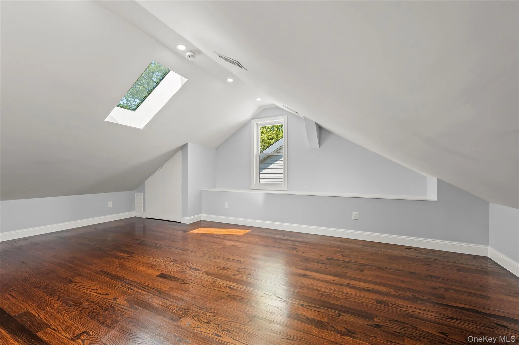 Spacious room featuring rich wood-finish flooring, a skylight, recessed lighting, and a window with louvered shutters Spacious room featuring rich wood-finish flooring, a skylight, recessed lighting, and a window with louvered shutters