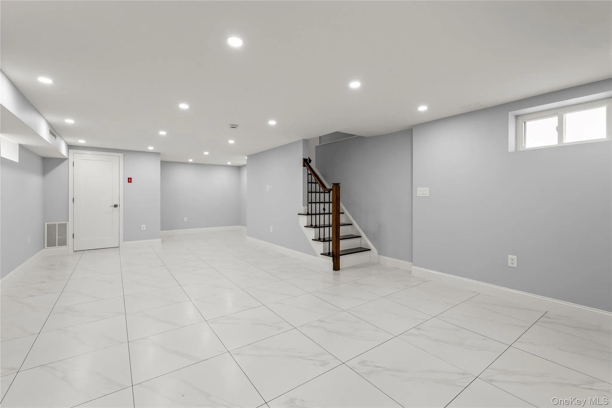 Expansive lower-level room featuring large format tile flooring, recessed lighting, and a window Expansive lower-level room featuring large format tile flooring, recessed lighting, and a window