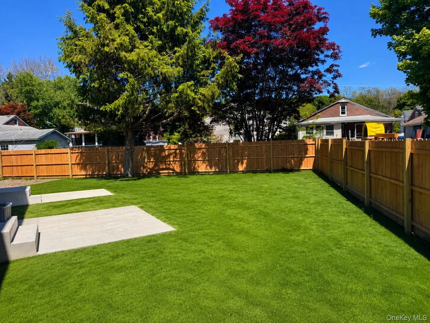 Expansive green lawn featuring a privacy fence, established trees, and two concrete patio areas Expansive green lawn featuring a privacy fence, established trees, and two concrete patio areas